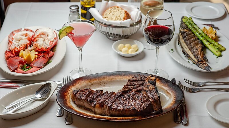 Multiple entrees with focus on steak with glass of red wine